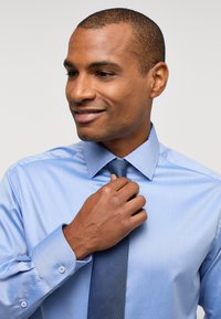 Camicia azzurro chiaro a maniche lunghe con bottoni, dal tessuto liscio, abbinata a una cravatta blu scuro a trama, con colletto a punta e dettagli ai polsini.