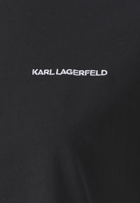 Juodas medvilninis marškinėliai trumpomis rankovėmis. Priekyje išsiuvinėtas tekstas "KARL LAGERFELD" balta spalva. Lygi tekstūra.