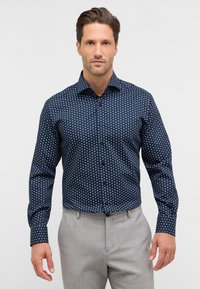 Camicia blu navy con un piccolo motivo circolare bianco. Maniche lunghe con polsini abbottonati, tessuto leggero e vestibilità sagomata.