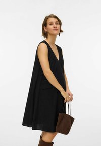 Melna bezapkakles kleita ar V-veida izgriezumu, divām priekšpusē esošām kabatām un plūstošu formu. Kopā ar nelielu brūnu zamšādas somiņu.