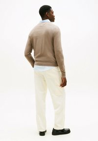 Maglione marrone da uomo in maglia indossato sopra una camicia collare azzurra, abbinato a pantaloni cargo crema e scarpe nere. Tessuto liscio e design aderente.