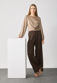 Beige satijnen top met lange mouwen en een geplooid voorpand, gecombineerd met hoge, losse bruine broek en tan gekleurde sandaaltjes met hak.