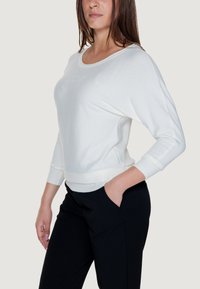 Maglione bianco a maniche lunghe con una vestibilità comoda, scollo rotondo e polsini a costine. Abbinato a pantaloni neri, realizzati in un tessuto leggero e morbido.