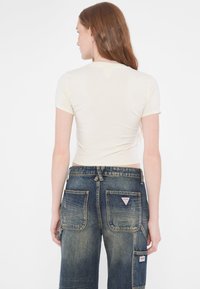 Top corto de manga corta en color crema combinado con unos pantalones cargo de denim azul desgastado de corte suelto, que cuentan con varios bolsillos y un parche de la marca en la parte trasera.