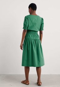 Grön bomulls-middress med puffärmar, smockad midja och flödande kjol. Enkelt design, inga synliga mönster, avslutad fåll. Bruna sandaler.