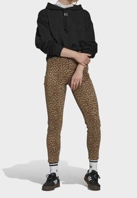 Sudadera con capucha negra, leggings de estampado de leopardo en marrón y beige, combinados con zapatillas negras y calcetines blancos con rayas negras.