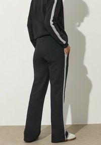 Schwarze Sweatpants mit lockerer Passform, ausgestattet mit grauen Seitenstreifen, aus weichem Stoff gefertigt. Mittlere Leibhöhe und klassischer Schnitt.