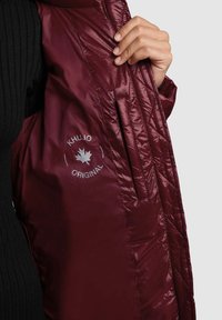 Burgundy quilted jacket interior shows a logo with "KHUJO ORIGINAL." Material is shiny and smooth, with side pockets visible.