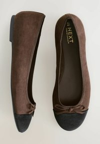 Braune Wildleder-Ballerinas mit einer schwarzen Wildleder-Zehenkappe, die eine Schleifendetail an der Vorderseite haben und eine glatte Gummisohle besitzen. Einfaches Design, vielseitige Farbe.