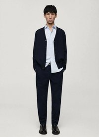 Marinblå cardigan över en ljusblå skjorta, parat med mörka byxor och svarta stövlar. Cardiganen har knappstängning och en avslappnad passform.