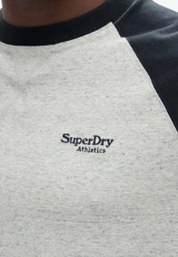 Graues und schwarzes Raglan-T-Shirt aus weichem Stoff, mit einem schwarzen "SuperDry Athletics"-Logo auf der linken Brustseite.