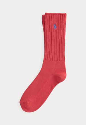 Chaussette rouge côtelée unique avec un logo brodé d’un joueur de polo bleu sur le mollet, pliée en haut sur fond blanc.