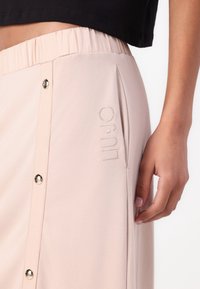 Helle rosa Rose mit einem elastischen Bund, Druckknöpfen und einem bestickten Logo auf der Seite. Weiches Material mit einer glatten Textur.