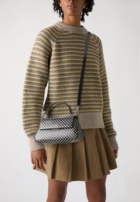 Håndtaske i sort og hvid med prikker, rund form, sølvhardware og kort håndtag, båret med en stribet sweater og nederdel.