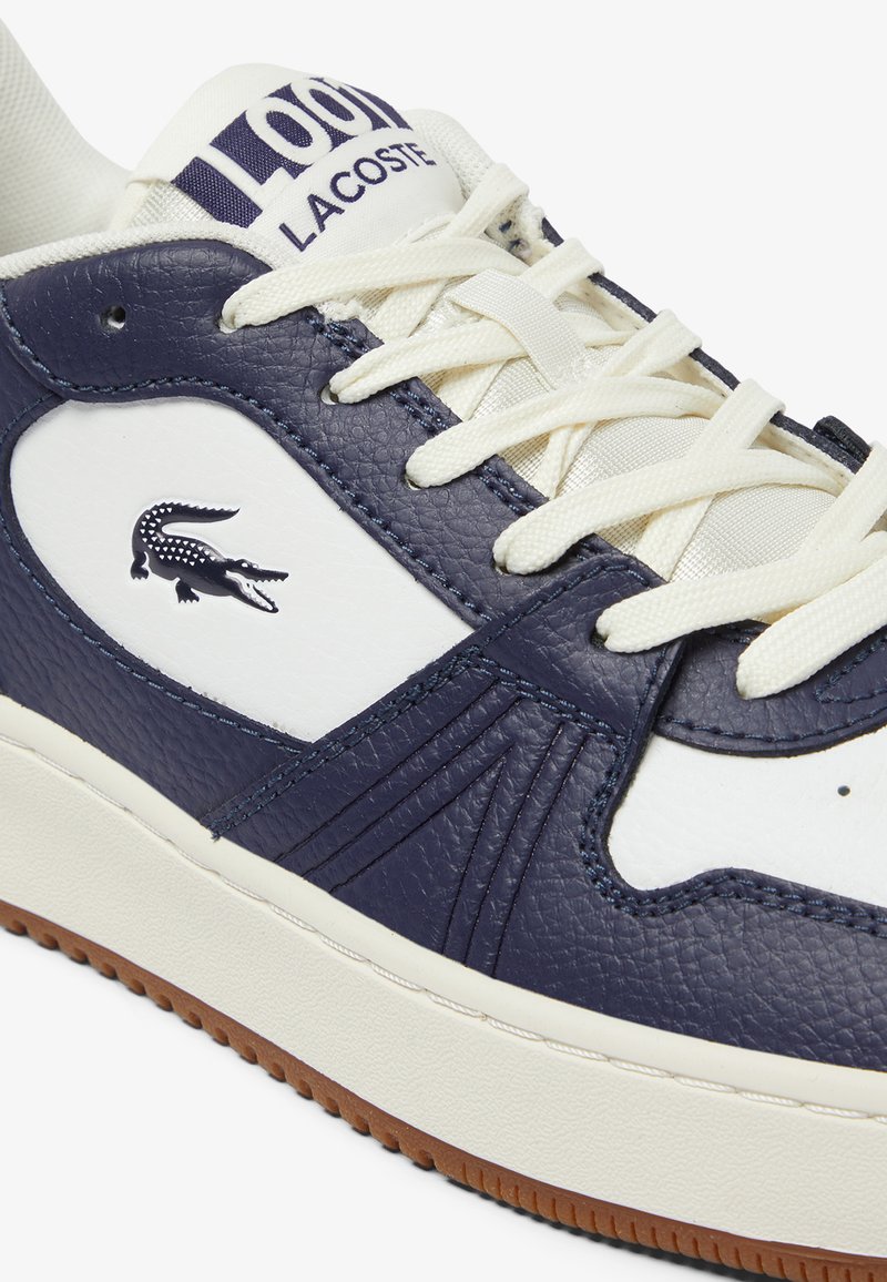 Marineblauer und weißer Leder-Sneaker mit strukturierten Akzenten, ausgestattet mit cremefarbenen Schnürsenkeln und einer braunen Gummisohle. Logo auf der Seite geprägt.