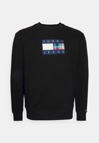 Černá mikina s kulatým výstřihem a žebrovanými manžetami, s vícebarevnou záplatu s logem Tommy Jeans na přední straně. Materiál z bavlněné směsi.