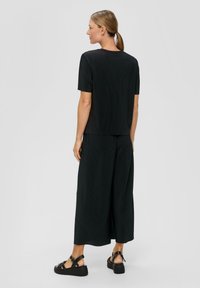 Czarna prążkowana bluzka z krótkim rękawem połączona z szerokimi czarnymi spodniami. Stylizacja charakteryzuje się luźnym krojem i jest uzupełniona czarnymi sandałami.