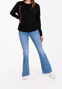 Sort sweatshirt med "PERFECT" skrevet i pink script langs siden, kombineret med vide blå jeans og hvide sneakers. Afslappet outfit.