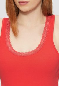 Rode tanktop met een ribbelstructuur en een scalloped kant halslijn, met een open scoopdesign rond de kraag.