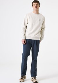 Grijze sweatshirt met ribgebreide manchetten, gecombineerd met marineblauwe broeken. Geweven stof en een eenvoudig logo op de borst. Schoeisel heeft een mix van kleuren.