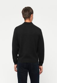 Svart strikket genser med ribbet rund hals, lange ermer og avslappet passform, med teksturert stoff og uten synlige mønstre.