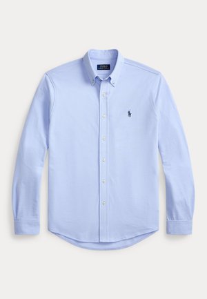 Lyseblå skjorte med lange ermer, knapper, knappet krage og liten brodert logo på venstre bryst.