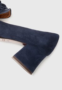 Navy blue suede block heel shoe with a pointed toe and a smooth texture; features a contrasting brown accent on the heel base.