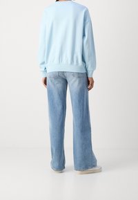 Light blue sweatshirt with dropped shoulders and ribbed cuffs, paired with light blue wide-leg jeans featuring a faded texture and back pockets.