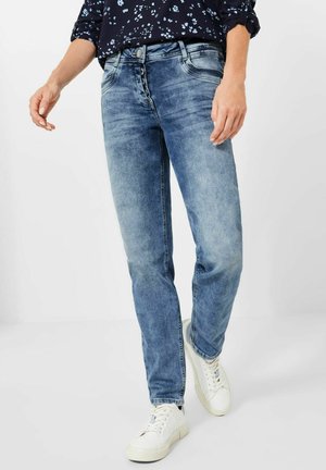 Vaqueros azul claro con un diseño de pierna recta, que presentan un cierre de cinco botones, textura de mezclilla y detalles de desvanecimiento mínimos. Combinados con zapatillas blancas.