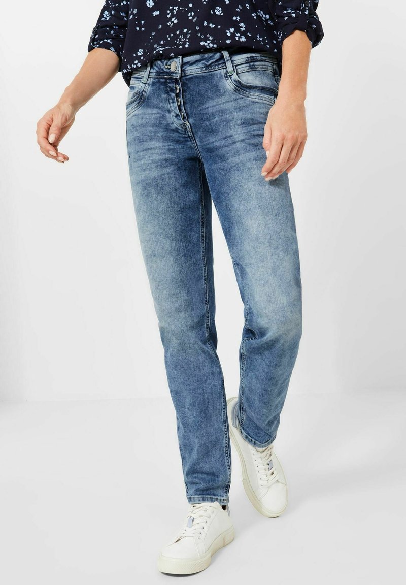 Světle modré džíny s rovnými nohavicemi, které mají pětici knoflíků na zapínání, denimovou strukturu a minimální detaily vyblednutí. V páru s bílými teniskami.