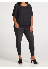 Svart kortärmad topp med texturerade axelaccents, elastisk nederdel; kombineras med svarta slim fit-jeans och svarta öppna skor.