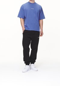 Camiseta azul de manga corta, pantalones deportivos negros y zapatillas blancas. La camiseta tiene un pequeño logo; los pantalones tienen un logo en el lateral.