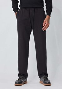 Pantalon noir, ample, avec taille élastique et cordon de serrage, en tissu doux ; style avec poches avant et jambes droites.