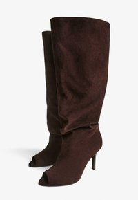 Hnedé semišové členkové čižmy s voľným dizajnom, otvorenou špičkou a tenkým vysokým podpätkom, predvádzajúce jemnú textúru a minimalistický štýl.