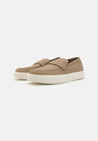 Kůže hnědé slip-on boty s texturovaným povrchem, s širokým pásem přes vršek a bílou gumovou podrážkou.