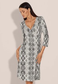 Schwarz-weißer Schlangenprint-Kleid mit V-Ausschnitt, Dreiviertelärmeln und Seitentaschen, hergestellt aus einem glatten, leichten Stoff.