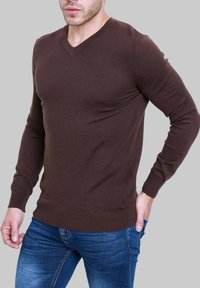 Pull marron en v en tricot côtelé, avec des manches longues et une silhouette ajustée, porté avec un jean en denim bleu.