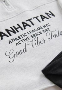 Helles graues Sweatshirt mit schwarzem gesticktem Text: "MANHATTAN ATHLETIC LEAGUE NYC AKTIV SEIT 1982" und "Good Vibes Today" in Schreibschrift.