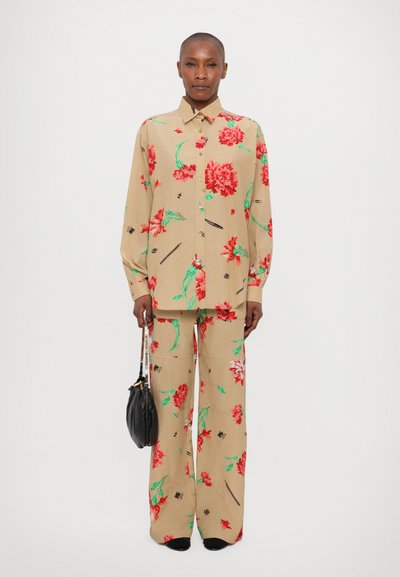Conjunto de dos piezas en beige con flores rojas, hojas verdes y acentos negros. Camisa de manga larga con cierre de botones, pantalones de pierna ancha.