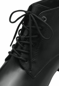 Botín de cuero negro hasta el tobillo con punta redonda, diseño con cordones, textura suave y ojetes de metal para los cordones. Detalles de costura a lo largo de los laterales.