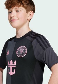 Schwarzes Fußballtrikot mit rosa Akzenten, ausgestattet mit einem Rundkragen, drei Streifen auf den Schultern und dem Vereinslogo auf der Vorderseite.