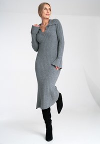 Szara, prążkowana dzianinowa sukienka z dekoltem w kształcie V i szerokim kołnierzem. Posiada długie rękawy z dopasowanymi mankietami oraz rozkloszowany dół, uzupełniona czarnymi botkami sięgającymi do kolan.