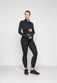 Svart langermet topp med glidelås og tettsittende svarte leggings. Stoffet ser glatt ut, designet for komfort, med et stilfullt, atletisk utseende.