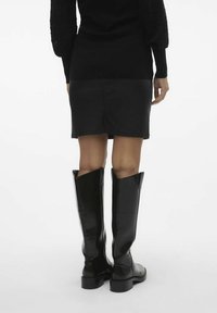 Svarta knähöga stövlar med en glänsande yta, spetsiga toppkanter och en kraftig sula. Bärs med en åtsittande svart läderkjol.