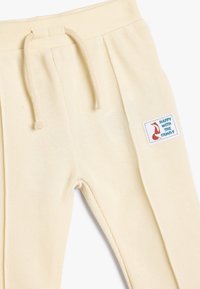 Ljust gula ribbade joggers med dragsko i midjan och en rektangulär lapp som står "GLAD MED FAMILJEN" tillsammans med en röd räv-grafik.