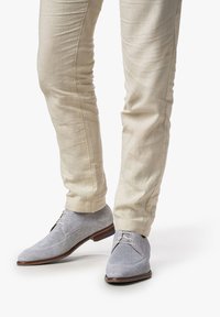 Scarpe grigio chiaro con dettagli in rete e accenti in pelle liscia, abbinate a pantaloni slim-fit color crema.