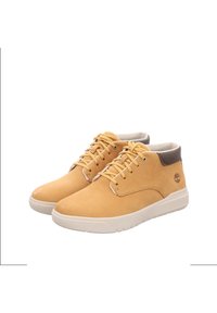 Zapatos de cuero de media caña en amarillo con un acabado texturizado. Cuentan con cordones redondos, un refuerzo en el talón de color marrón en contraste y una suela de goma blanca.