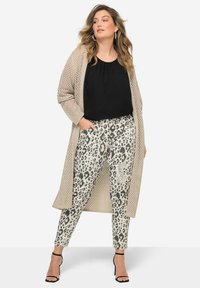 Cardigan en tricot beige, haut noir et pantalon gris clair avec imprimé léopard noir. Talons aiguilles noirs à lanières. Tissu texturé et coupe décontractée.