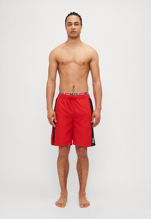 Shorts de bain rouges avec un panneau latéral noir, taille élastique avec la marque "DIESEL" en blanc, et cordon de serrage. Tissu lisse, design longueur genoux.