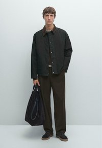 Dark green jacket with brown collar, brown pants, and dark bag. Textured fabric, relaxed fit, featuring snap buttons and side pockets.